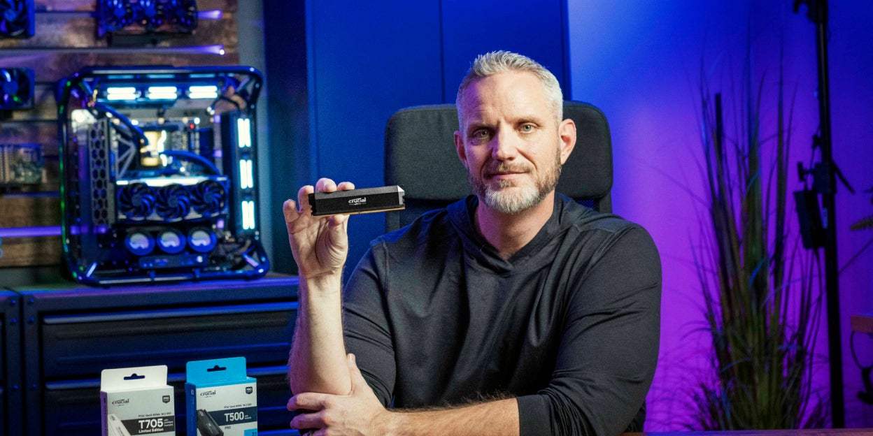 Jason Langiven sitting at a desk and holding up Crucial DRAM to the camera. A T705 and T500 box are placed next to him.