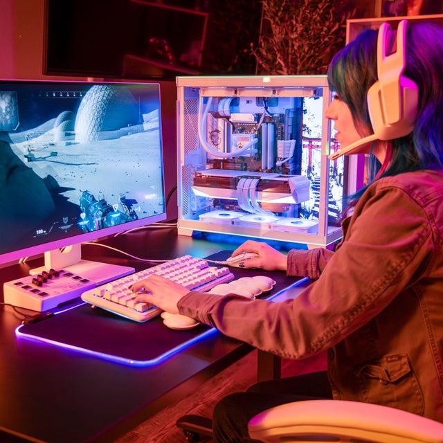 A girl gamer sitting at desk playing video games with pink headphones and pink lights