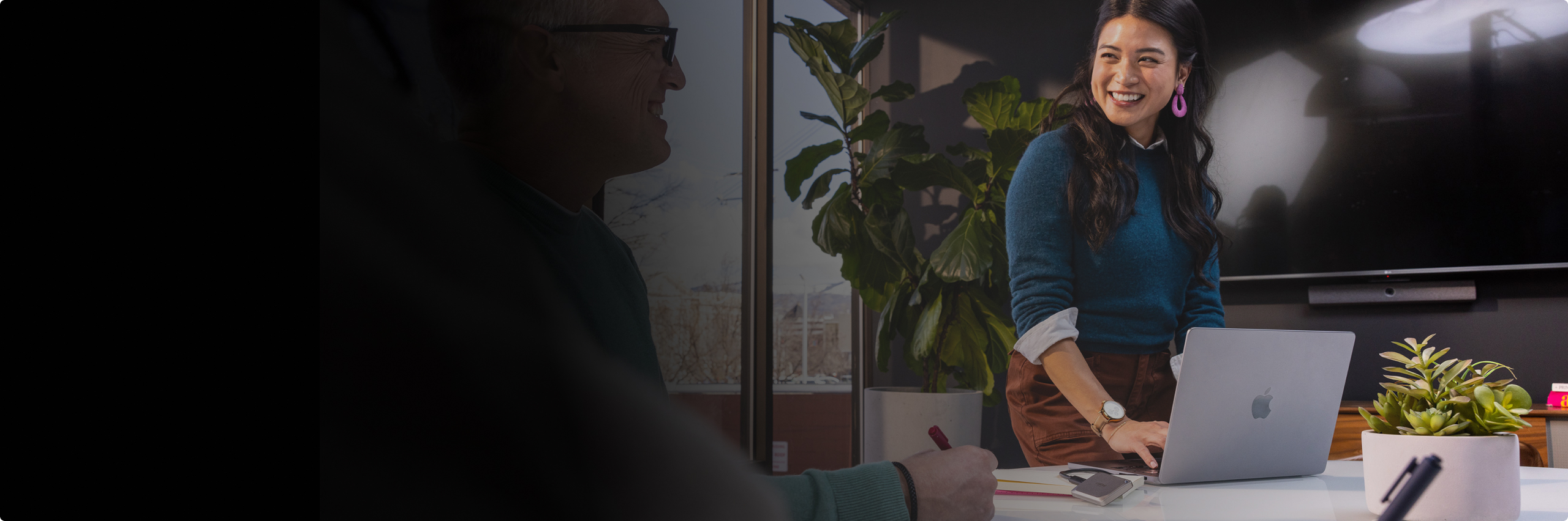 A woman working on a laptop with a phone in her other hand and a Crucial external SSD connected to the laptop via USB.