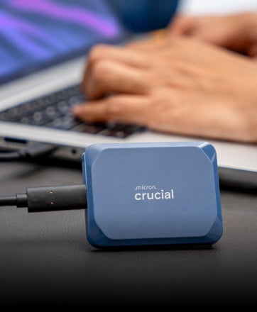  A Crucial X9 Pro 4TB Portable SSD set vertically on a desk in front of a laptop.