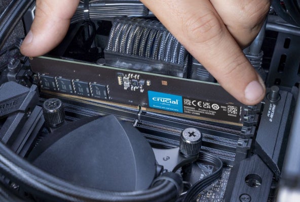  Fingers pushing down on a Crucial RAM module to secure it into a DIMM slot on a motherboard.