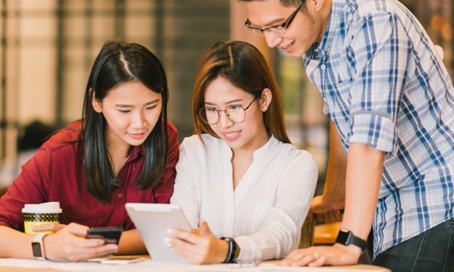 A woman writing on a whiteboard wall with two male co-workers looking over her shoulder